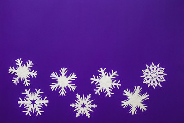 White paper snowflakes different shapes and sizes on violet background. Top view.