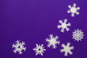 White paper snowflakes different shapes and sizes on violet background. Top view.