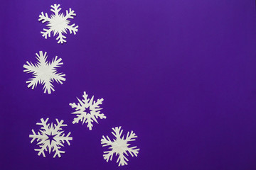 White paper snowflakes different shapes and sizes on violet background. Top view.