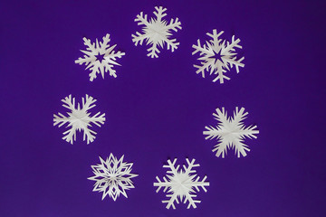 White paper snowflakes different shapes and sizes on violet background. Top view.
