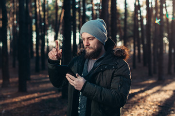 Portrait of adult man walking in the pine forest with digital tablet.