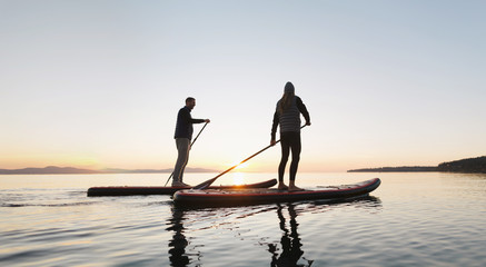 Couple stand up paddle boarding together at sunrise