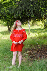 Cute blond young girl posing in a russian traditional red dress near fir tree