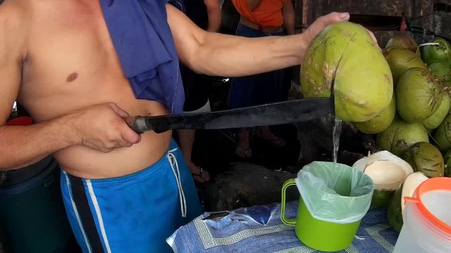Young coconut vendor punch fruit to extract buko juice into plastic bag