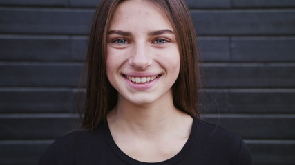 An attractive young lady straightens her hair and smiles outdoors. Close-up shot