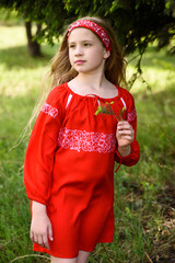 Cute blond young girl posing in a russian traditional red dress near fir tree