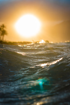 Scenic Tropical View of Waves Crashing from Low Perspective near water with Sun Rays coming through Clouds and Palm Tree Silhouette on Maui Hawaii