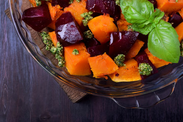 Roasted pieces of pumpkin and beetroot with pesto sauce in a glass dish. Vegetarian meal