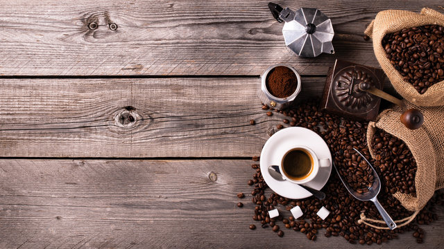 on the rustic wooden table a cup of hot coffee, a vintage coffee grinder, an Italian moka and coffee beans. High angle view