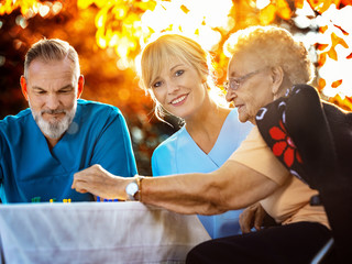Pfleger spielen mit Seniorin im Garten ein Brettspiel