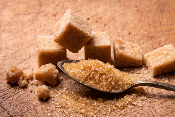 In the foreground, raw cane sugar crystals in the spoon. In the background some sugar cubes