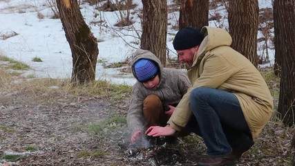 Family having fun at picnic in winter frosty wood outside. Father and child on winter walk outdoors arranging small bonfire. Family portrait. Dad and son happy winter adventures concept.
