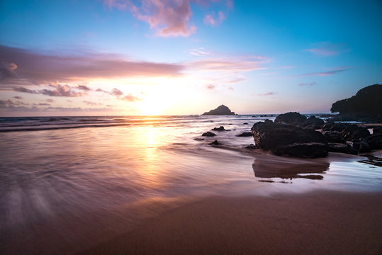 Colorful Pastel Sunrise Sky at Dawn with Sun Coming Over Ocean Horizon Relaxing Tropical Island Paradise of Silky Smooth Water on Sandy Beach with Mountain Background and Pink Clouds on Maui Hawaii