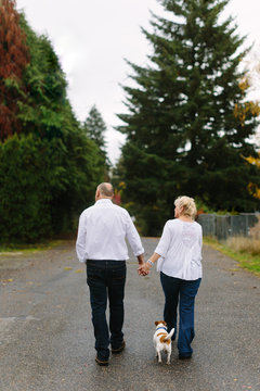 Older Couple Walking Down Path With Little Dog