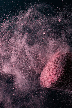 Make-up brush with pink face powder against dark background
