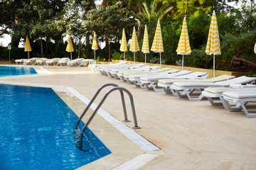 Swimming pool with stair and wooden deck at hotel. Grab bars ladder in the blue swimming pool....