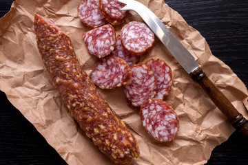 dry sliced salami on kraft paper and dark wooden background