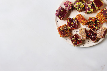 Obraz na płótnie Canvas Variety of traditional turkish dessert Turkish Delight different taste and colors with rose petals and pistachio nuts on ceramic plate over white marble background. Flat lay, space
