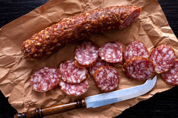 dry sliced salami on kraft paper and dark wooden background