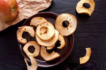 apple chips on a dark wooden background and a fresh whole apple