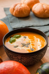 Pumpkin soup puree with cream and pumpkin seeds on the background of whole pumpkins of different colors. The surface of the textile