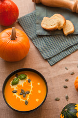 Pumpkin soup puree with cream and pumpkin seeds on the background of whole pumpkins of different colors. The surface of the textile