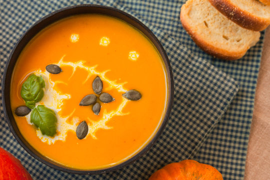 Pumpkin soup puree with cream and pumpkin seeds on the background of whole pumpkins of different colors. The surface of the textile