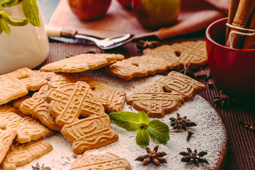 Speculaas Christmas cookies on a wooden board sprinkled with powdered sugar with mint leaves and oriental spices
