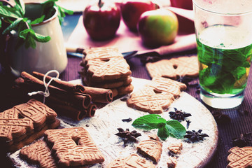 Speculaas Christmas cookies on a wooden board sprinkled with powdered sugar with mint leaves and oriental spices. Tea with mint, lemon and oriental spices