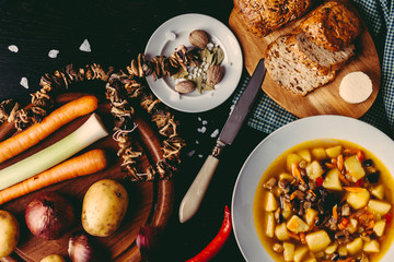 Homemade mushroom soup of dried porcini mushrooms with potatoes, bread and other vegetables on a dark wood table. Vegetables and spices