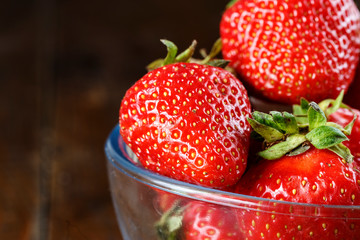 Ripe strawberries in a glass container on a wooden background.