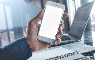 Young businessman holding blank smartphone with workplace.Business planning.