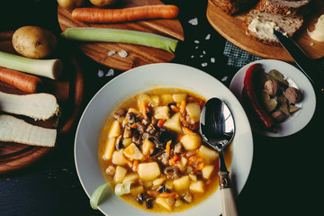 Homemade mushroom soup of dried porcini mushrooms with potatoes, bread and other vegetables on a dark wood table. Vegetables and spices