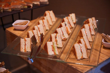 sandwiches filled with fish and vegetables lie on a glass plate, next to the tongs