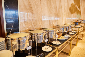 hot dishes on a buffet table in silvery thermo pans on a glass table - Swiss table