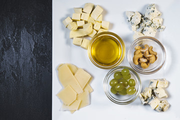 Delicious fresh cheese set with nuts, honey and grapes in a white plate on a black stone table background