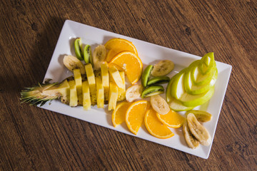 sliced fruits in a white plate are on the table - proper nutrition, raw foods, vegetarianism, pineapple, apple, orange, banana and kiwi