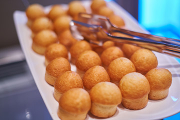 mini cupcakes, muffins on a white plate - tongs are on the cupcakes