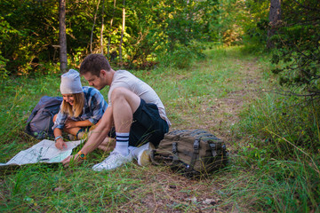 Naklejka na ściany i meble Young couple examining the map inside the forest. Hiking concept in the mountain in summer