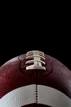 American football and sports night event concept with close up on the laces of a leather ball isolated on black background with dramatic light lit from one side and copy space for text