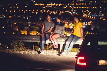 Friends sittinig on road guardrail at night