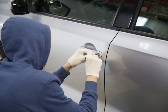 The hijacker tries to break into the car with a lock pick. Car thief, car theft.