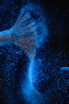 Make-up brushes with blue face powder against dark background