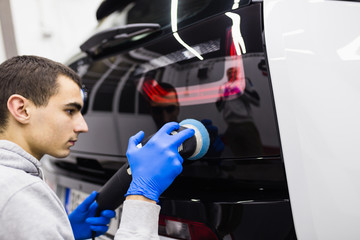 Car detailing - Worker with orbital polisher in auto repair shop. Selective focus.