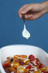 Unrecognizable person pouring yogurt and scallion sauce in sweet potato and cherry tomato salad. Selective focus. 
