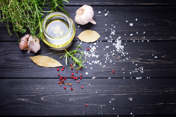 Bottle with olive oil with herb and spices ob black wooden background.