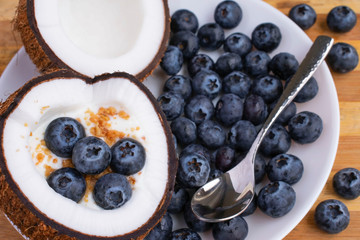 Healthy breakfast or snack in cut half coconut on wooden background. Yogurt in coconut bowl with blueberries and granola.