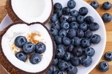 Healthy breakfast or snack in cut half coconut on wooden background. Yogurt in coconut bowl with blueberries and granola.