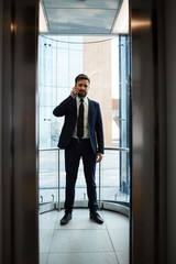 Contemporary businessman in formalwear talking by smartphone inside office