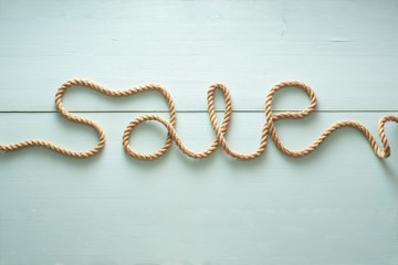 sale inscription is written using a rope made of jute illuminated with a side light on a green wooden background.